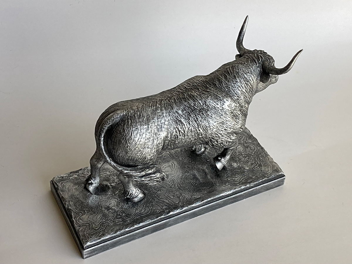 Silver-painted bull figurine on a decorative base, showing the textured surface and oxidized metallic finish